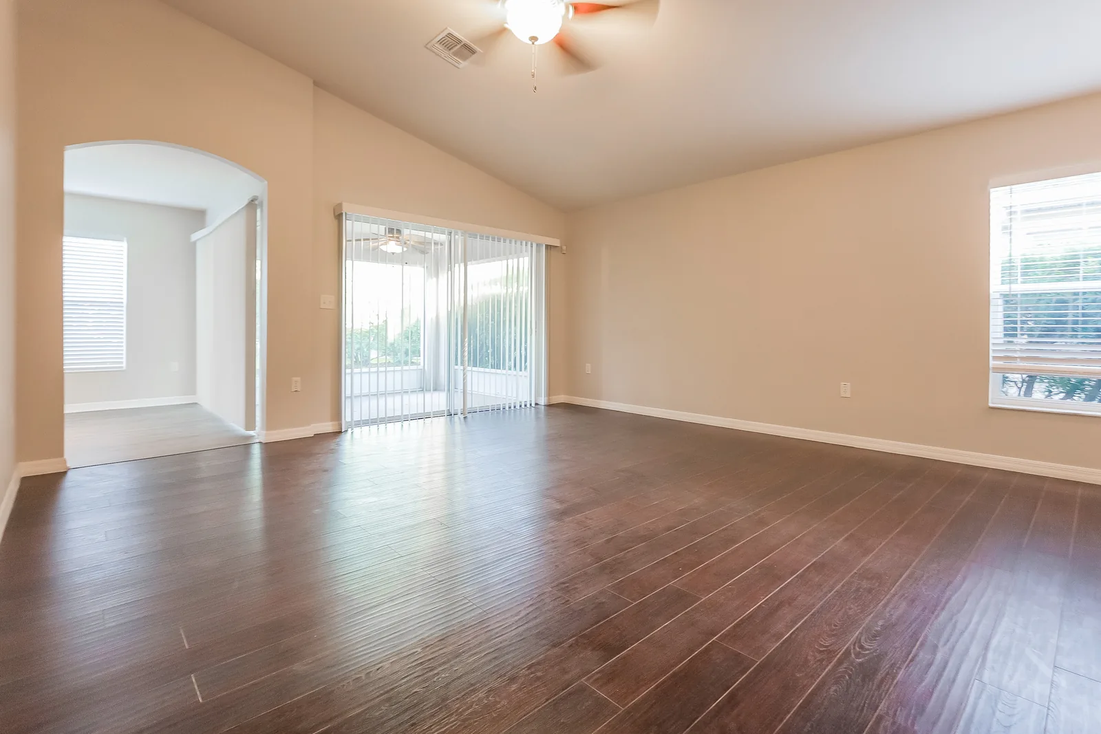 Living room at the Tee Shot Drive home with a vaulted ceiling, dark wood-look flooring, and sliding glass doors to the lanai